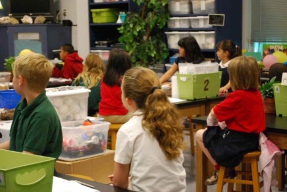 Kinder sitzen an Tischen in einem Klassenraum und arbeiten mit verschiedenen Materialien.