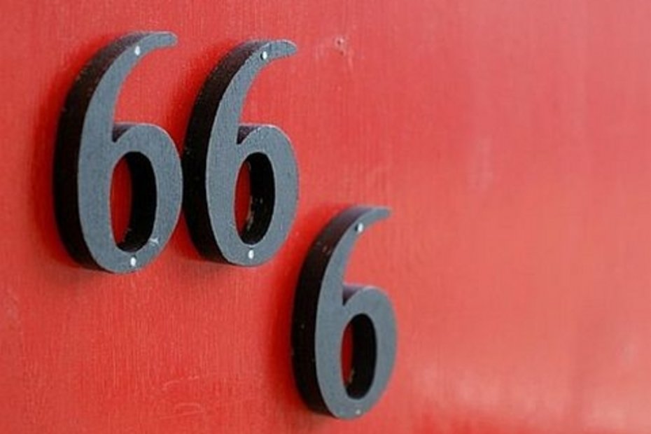 Drei schwarze Hausnummern „6“ sind versetzt auf einer roten Wand angebracht.
