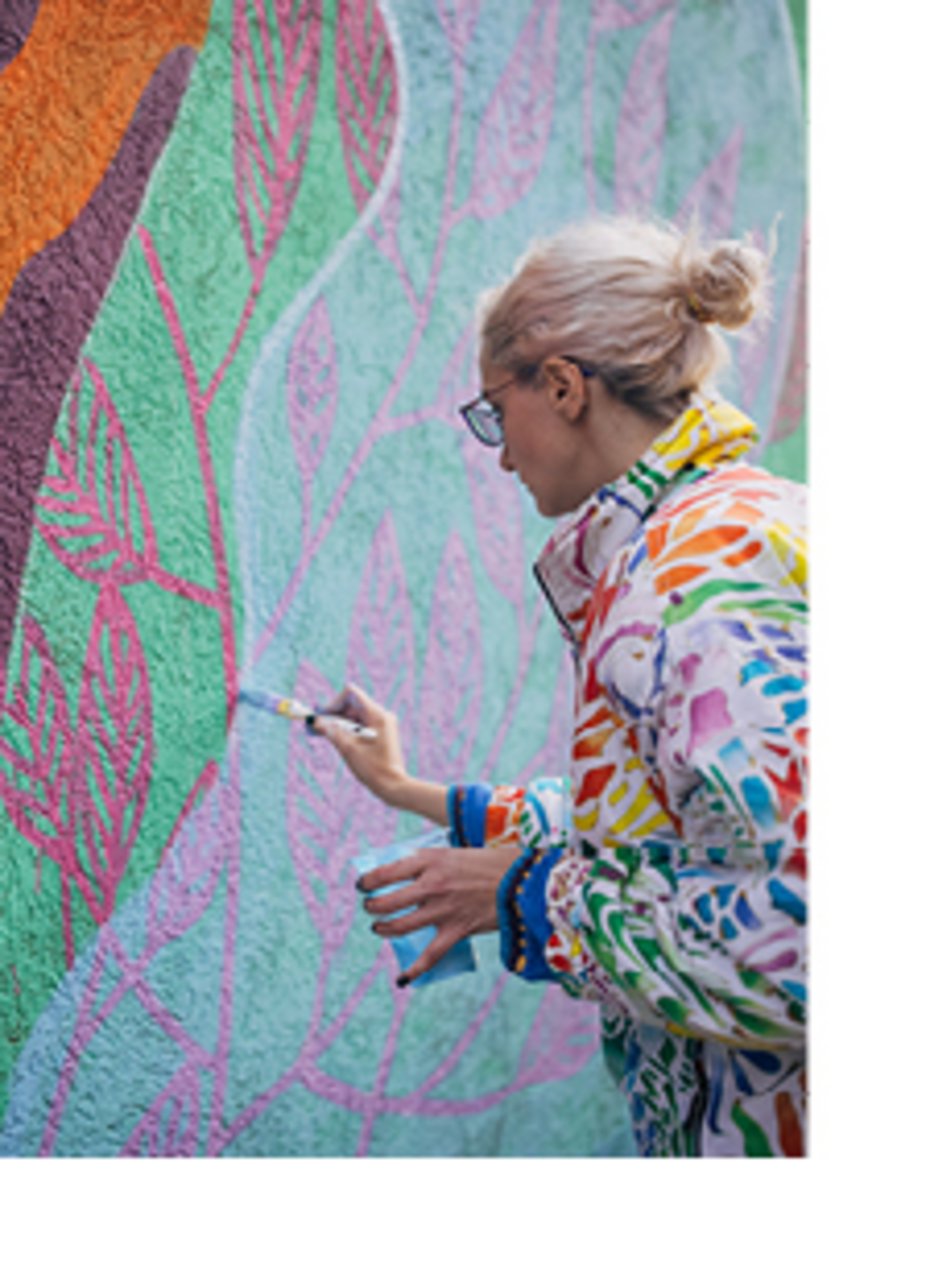 Kuenstlerin malt buntes Gemälde an eine Wand